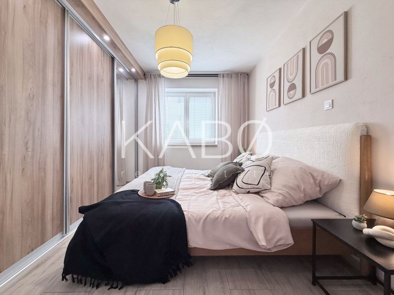 A bedroom in a two-room apartment with a wooden decor floor, a large built-in wardrobe, and wall decorations.