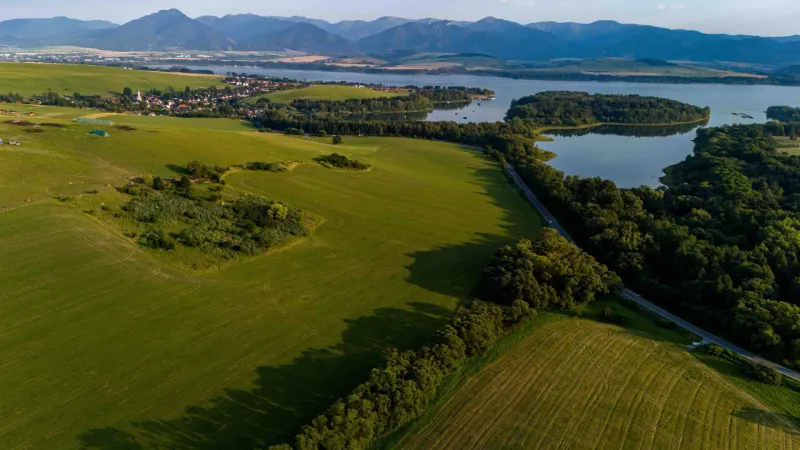 Liptovský Trnovec offers extensive greenery with a lake, surrounded by forest vegetation and fields.