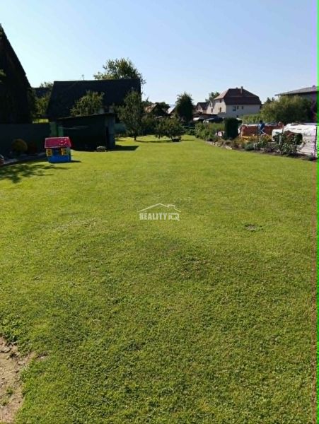 A flat lawn on a residential plot in Ovčiarsko with surrounding houses in the countryside.