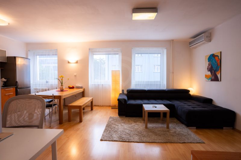 Living room of a 4-room apartment with a sofa, dining table, and wooden decor flooring.