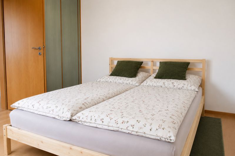 A bedroom with a double bed, pillows in a two-room apartment on a floor with a wooden decor.