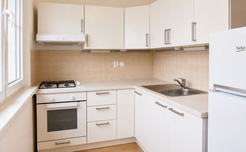 A kitchen with white cabinets and appliances in a 2-room apartment, floor with wood decor.