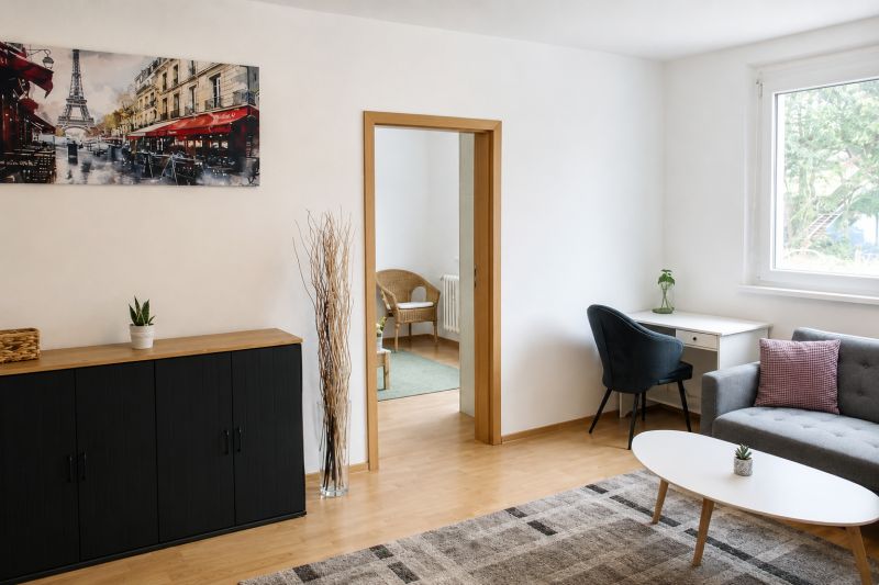 Living room in a two-room apartment with a wooden-patterned floor and a picture of Paris.