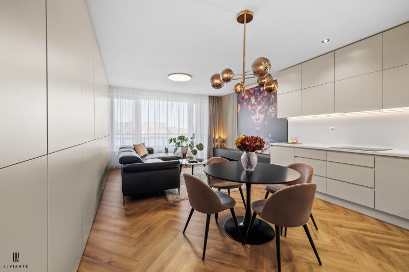 Interior of a 3-room apartment with stylish lighting, a black sofa, decorative art, and a wooden-patterned floor.