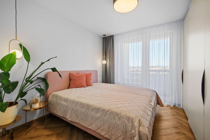 A bright bedroom with a bed, a plant, and a wooden decor floor in a 3-room apartment.