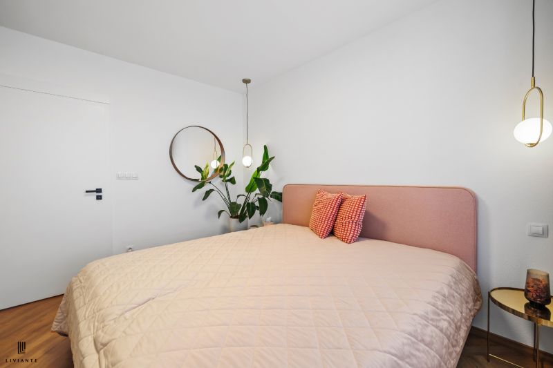A bedroom in a 3-room apartment with a plant, a pink bed, and wooden decor.