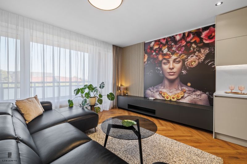 Living room with a leather sofa, artistic wallpaper, and wood-patterned flooring in a three-room apartment.