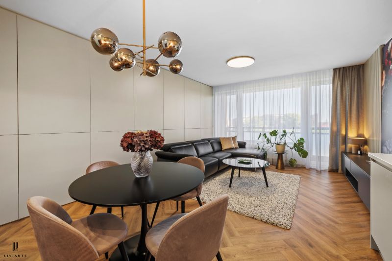 A living room in a three-room apartment with a wooden decor floor, a large window, and elegant lighting.