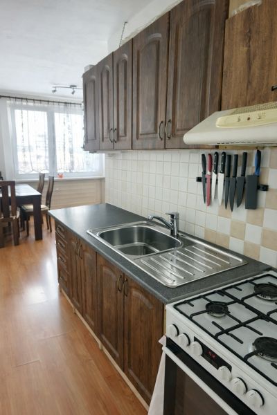 A kitchen in a 3-room apartment with a wooden decor floor and stylish cabinets.
