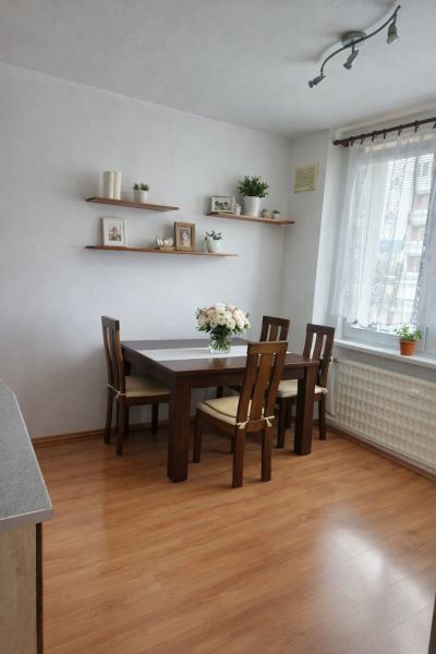 Dining area with a table, chairs, and shelves on a wooden floor in a 3-room apartment.