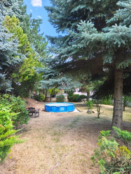 A garden in Mankovce with a swimming pool and a bench in the shade of trees near a family house.