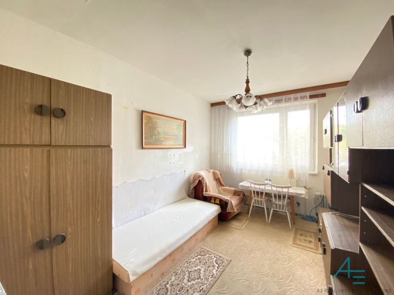 A room in a 4-room apartment with simple furniture and a carpeted rug.