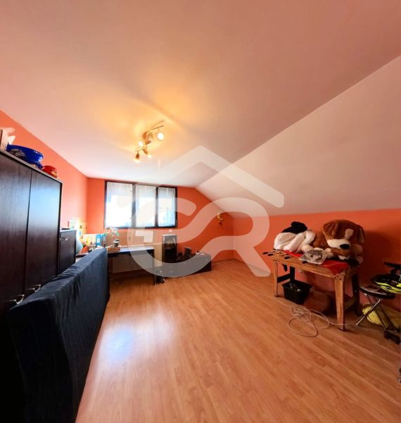 Attic room with a desk, sofa, and wooden decor flooring.