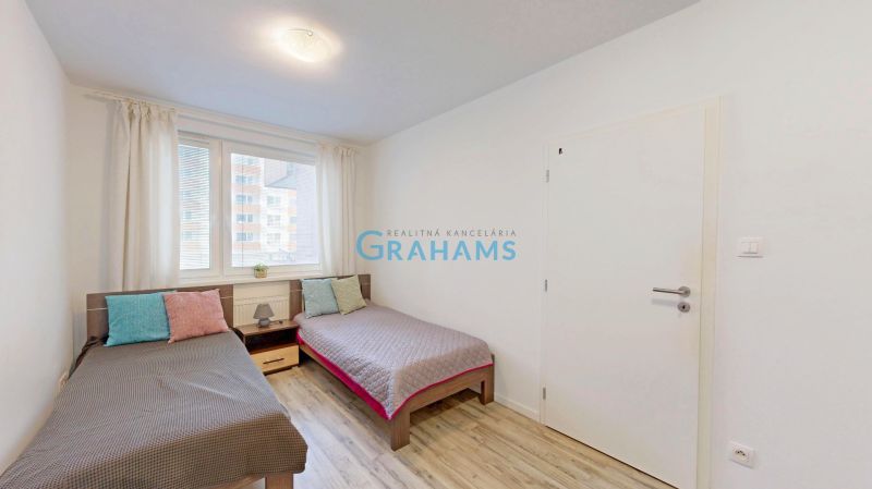 Two beds with colorful pillows and a wooden decor floor in a three-room apartment.