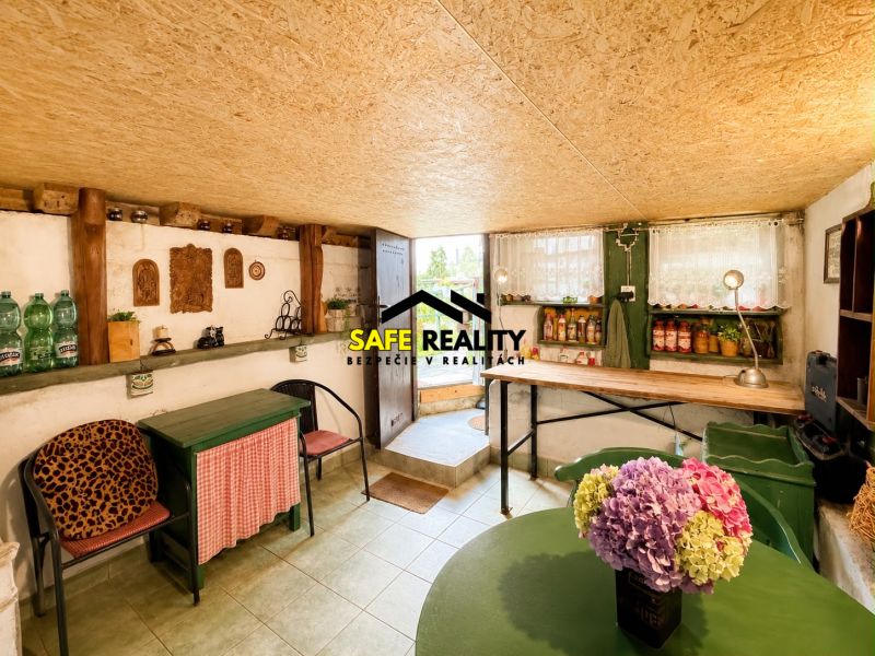 The interior of a cottage with rustic furniture, shelves, and a vase with flowers.