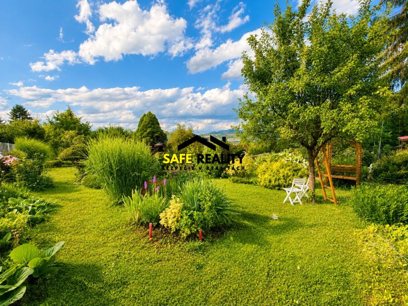 A garden near a cottage in Žilina with trees, flowers, and white garden furniture.