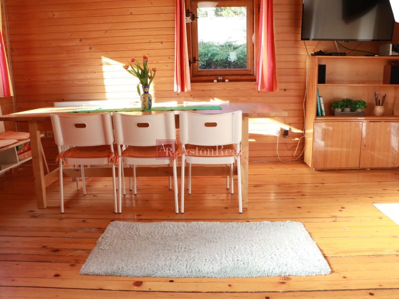 A wooden interior of a cottage with a dining table, white chairs, and a floor with a wooden decor.