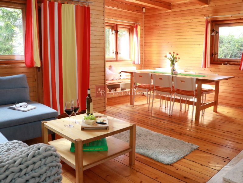 A cabin with wooden decor, comfortable furniture, a dining table, and a glass of wine.