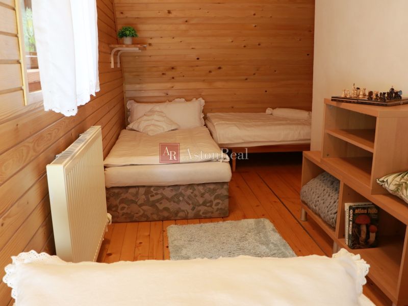 Wooden paneling of the room in the cottage, two beds, floor with wooden decor, bookshelf.