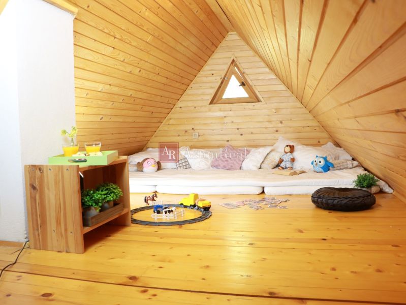 The attic space of the cottage with a wooden decor floor contains mattresses, toys, and a table.