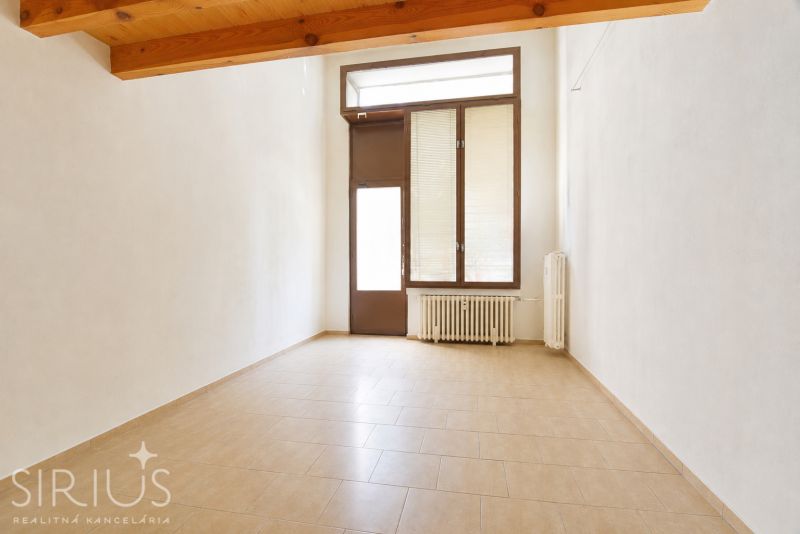An empty commercial space with a window and a radiator, floor with wooden decor.