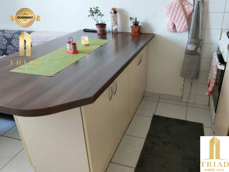 A kitchen unit with an island in a studio apartment, white tiles and decorations.