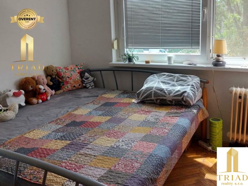 A bedroom in a studio apartment with a bed and a pile of stuffed toys on the bed.
