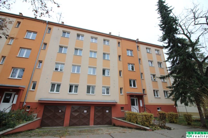 Apartment building in Trnava with a colorful facade, garages, and surroundings with trees.