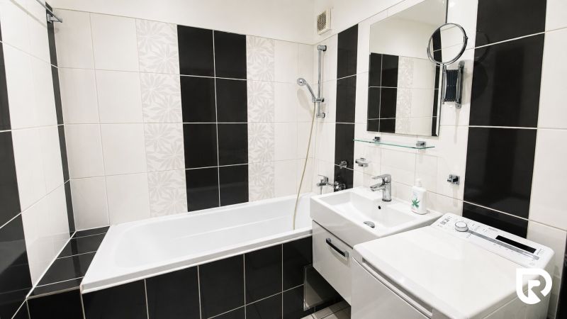Bathroom with a bathtub, sink, and washing machine in a 2-room apartment. Black and white tiles.