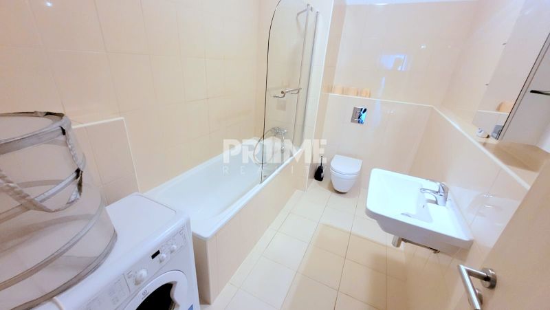 A bathroom with a bathtub and a washing machine in a 2-room apartment, light tiles, sink.