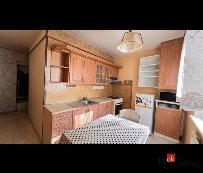 A kitchen with wooden decor, cabinets, and a dining table in a two-room apartment.