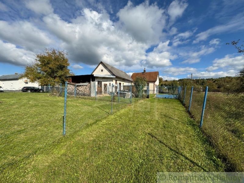 A family house in Volica surrounded by a green lawn and a blue fence under a blue sky.