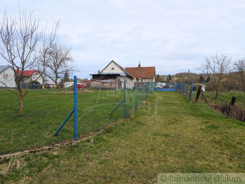A family house in the village of Volica with a lawn and a blue fence, without leaves on the trees.