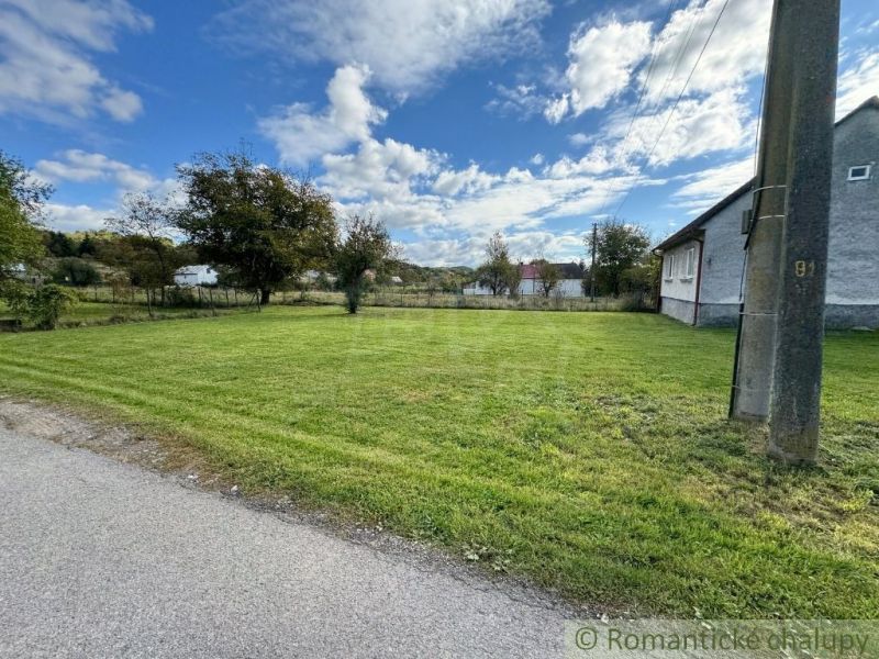 A grassy plot near a family house in Volica surrounded by trees and a clear sky.