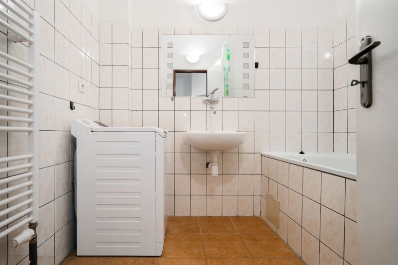 Bathroom in a 2-room apartment with a washing machine, sink, bathtub, and white tiles.