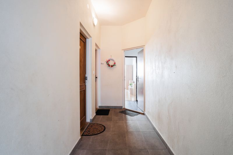 A hallway in a 2-room apartment with tiles, an entrance door, and a decorative wreath on the wall.
