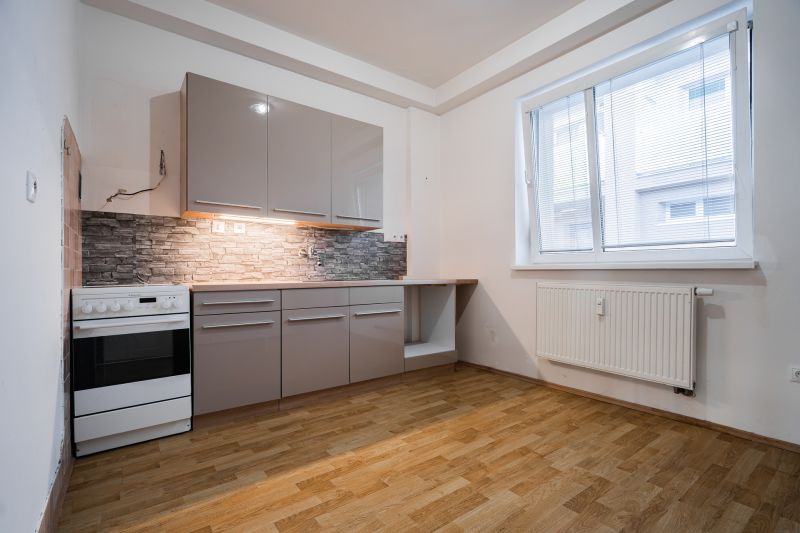 A kitchen in a 2-room apartment with gray cabinets, tiled backsplash, and a wooden decor floor.