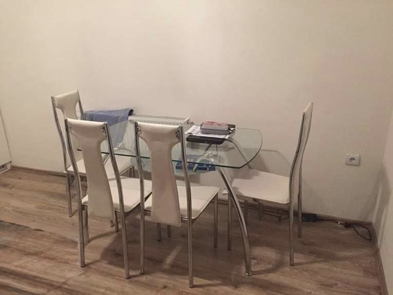 Glass dining table with white chairs on a floor with wood decor.