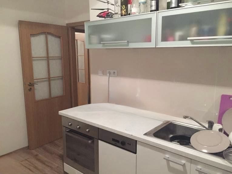 A kitchen in a 2-room apartment with a sink, stove, and storage cabinets.