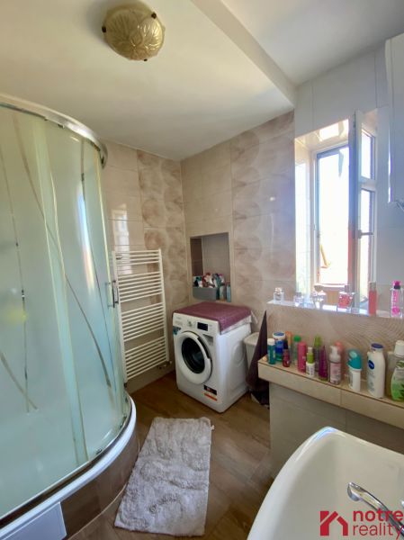 The bathroom with a washing machine and a shower in the studio apartment has a floor with a wooden decor.