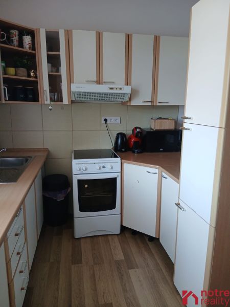 A kitchen in a studio apartment with a wooden decor floor and white cabinets.