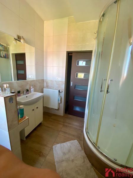Bathroom with a corner shower, light ceramic tiles, and a sink in a studio apartment.