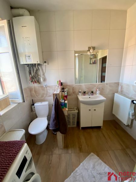 A bathroom with a sink, toilet, washing machine, and wooden decor flooring in a studio apartment.