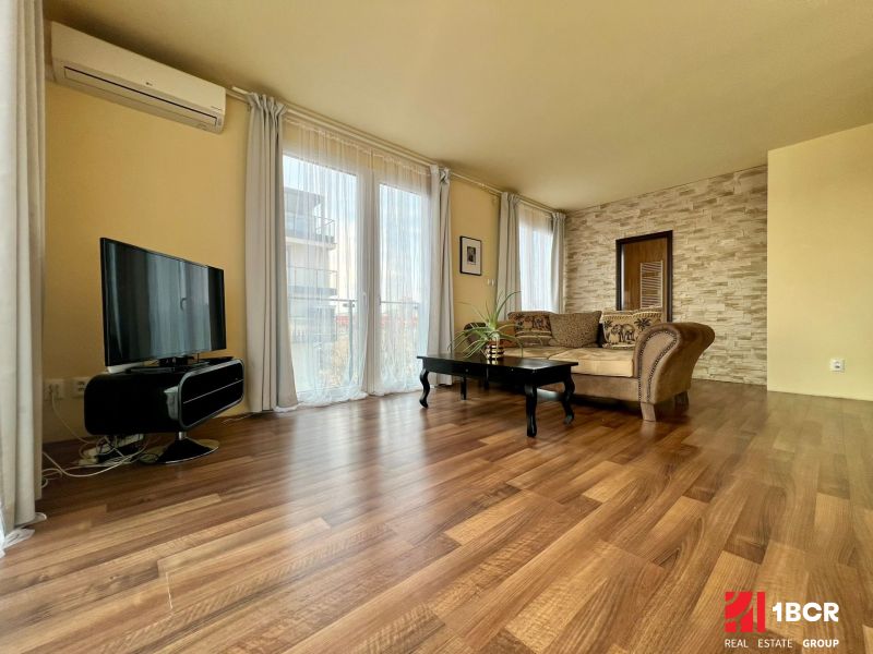 Living room in a two-room apartment with a wooden decor floor, a television, and a comfortable sofa.