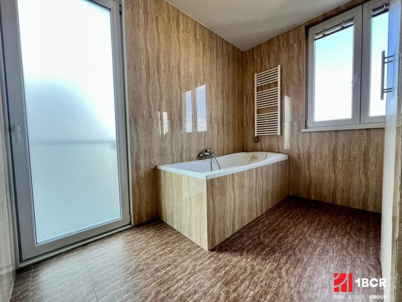 A bathroom in a 2-room apartment with a bathtub, a window, and glass doors.