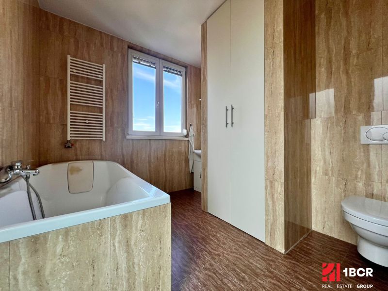 A bathroom with a bathtub and a wooden decor floor in a 2-room apartment.