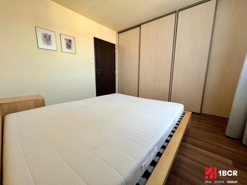 Bedroom with a double bed, built-in wardrobe, and wooden decor flooring in a 2-room apartment.