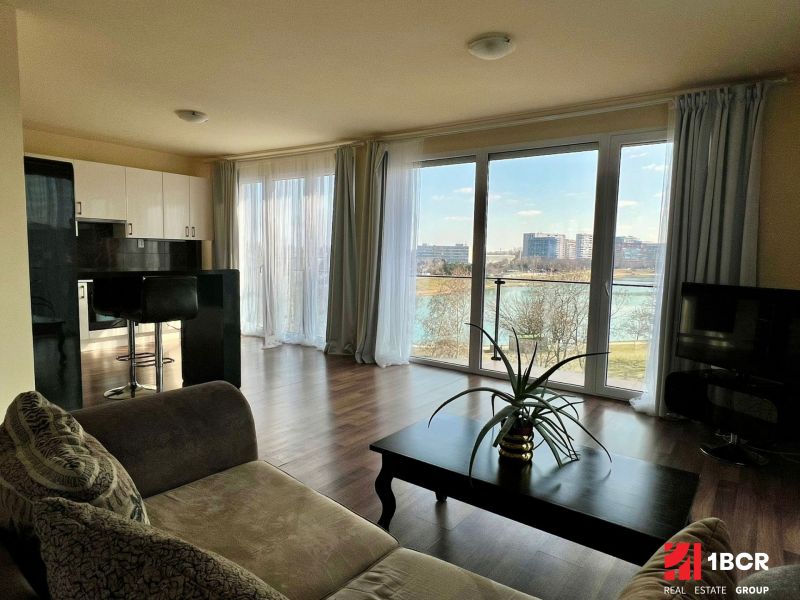 Living room in a 2-room apartment with large windows and a wooden decor floor.