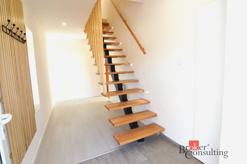 A hallway in a 2-room apartment with an open staircase and a wooden decor floor.