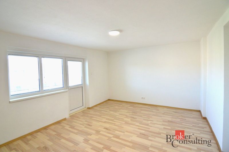 A bright room in a 2-room apartment with a wooden decor floor and large windows.